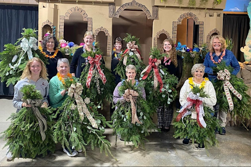 Group of women holding decorated wreaths in front of a castle-like structure.